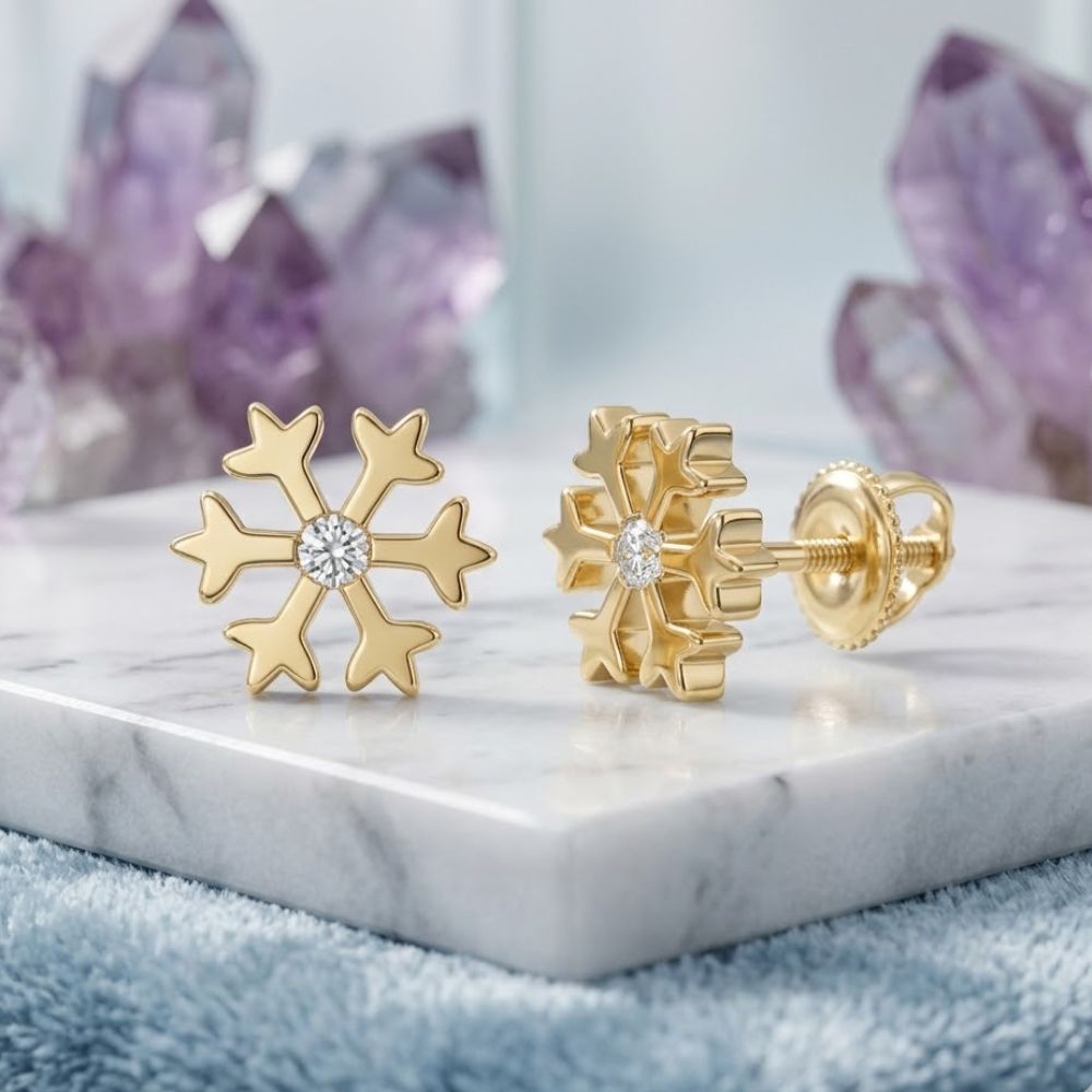 The 10k Yellow Gold Diamond Snowflake Earrings 1/20 CTTW are displayed on a white marble surface with purple crystals in the background.