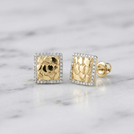 The 10K Yellow Gold Diamond Nugget Square Earrings feature a textured, hammered surface reminiscent of diamond nugget designs, bordered by small clear stones and beautifully showcased on a white marble surface.