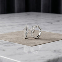 The 1/4 CTW Natural Diamond Fashion Hoop Earrings in 10K Gold are displayed upright on a square beige mat atop a white marble surface, set against a dark, softly blurred background.