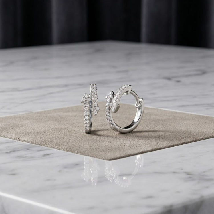 The 1/4 CTW Natural Diamond Fashion Hoop Earrings in 10K Gold are displayed upright on a square beige mat atop a white marble surface, set against a dark, softly blurred background.