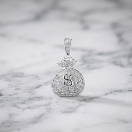 Showcased on a white marble surface, the Diamond Money Bag Pendant 1 CTTW Sterling Silver gleams with a sparkling dollar sign and is adorned with 1 carat total weight of shimmering stones.