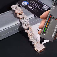 A hand holds a diamond tester to the Silver Moissanite Flower Infinity Bracelet with sparkling flower accents and large interlocking links on a silver box, with a certification card in the background.