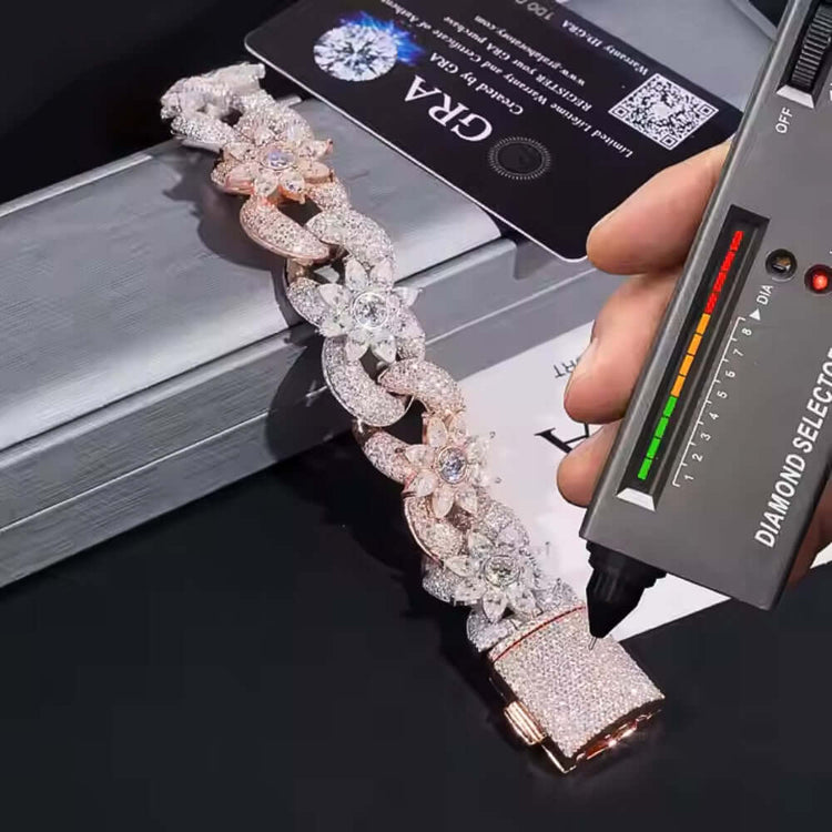 A hand holds a diamond tester to the Silver Moissanite Flower Infinity Bracelet with sparkling flower accents and large interlocking links on a silver box, with a certification card in the background.