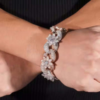 A close-up of two hands crossed at the wrists, wearing the Silver Moissanite Flower Infinity Bracelet with sparkling floral and crescent designs, set against a dark background.
