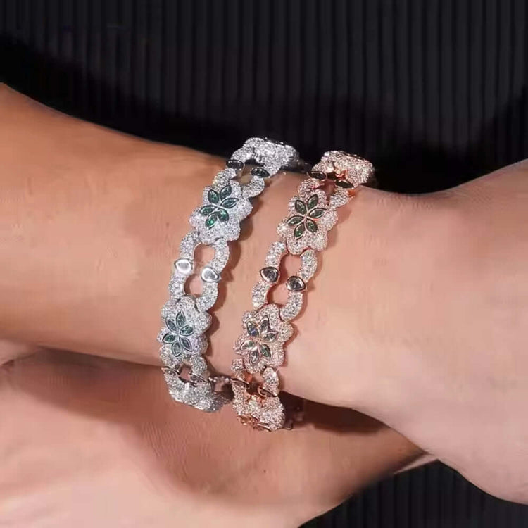 Two wrists showcase Flower Design Silver Moissanite Bracelets—one in sterling silver, one in rose gold—each with floral motifs, green gemstone centers, and sparkling stones. Set against a dark, textured fabric backdrop.