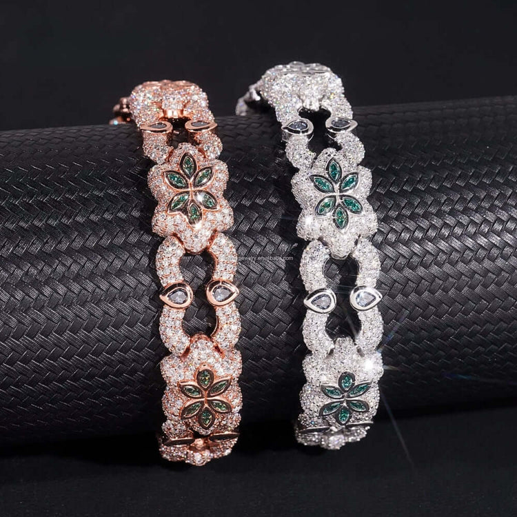 The Flower Design Silver Moissanite Bracelet, featuring sparkling stones and green gem flower accents, is draped over a textured black cylinder.