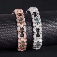 The Flower Design Silver Moissanite Bracelet, featuring sparkling stones and green gem flower accents, is draped over a textured black cylinder.