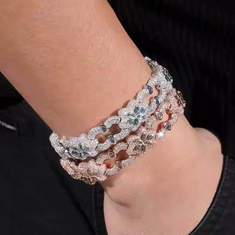 A close-up of a wrist in black clothing wearing three glittering bracelets, including the Flower Design Silver Moissanite Bracelet with intricate floral motifs and sparkling stones in silver, rose gold, and gold tones.