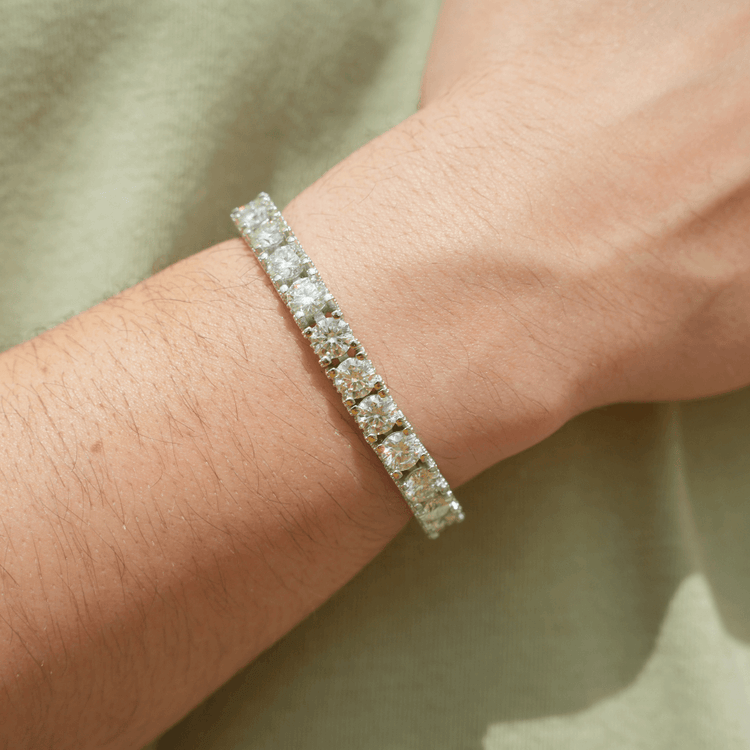 A close-up of a wrist adorned with the Fully Iced Out Moissanite Tennis Bracelet, sparkling brilliantly against a light green shirt background.