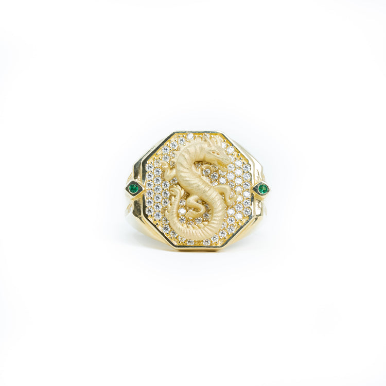 The Dragon Men Ring - 10k Solid Gold features an octagonal face with a raised dragon design, small clear gemstones, and two green gemstones on the sides, all set in solid gold.