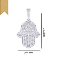 The Moissanite Hamsa Symbol Charm Pendant features an engraved eye design with small clear stones around the border and measures 49.4mm tall by 29.4mm wide, accented by a gold ribbon in the top left corner.