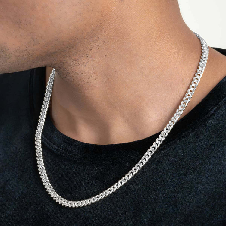 A close-up shows a person wearing the Hollow White Gold Cuban Link Chain 3mm - 7mm over a black shirt, highlighting the polished finish and bold look across the lower face, neck, and upper chest.