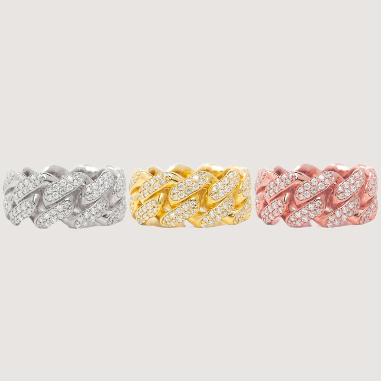 Three thick 14k solid gold Cuban link rings, each 10mm wide and iced out with sparkling diamonds, are displayed in silver, gold, and rose gold finishes. These dazzling rings shine brilliantly against a plain light background.