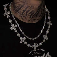 A person with neck tattoos in a dark shirt wears two layered silver chains: one is the Iced Out Moissanite Rosary Ball Chain featuring VVS Moissanites and cross pendants, the other a simple 925 sterling silver chain.