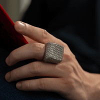 A hand holds a red object, showcasing the Iced-Out Square Cluster Ring—13.1 CT lab diamonds set in 14k gold—for an eye-catching sparkle.