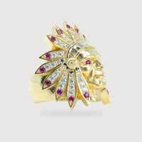 The Indian Men's Medium Ring - 10k Gold features a face with a feathered headdress, set with clear and red gemstones on the feathers. The ring is showcased against a plain light gray background.