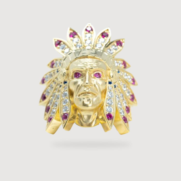 The Indian Men's Medium Ring - 10k Gold features a face wearing a feathered headdress and is adorned with white and pink gemstones, set against a plain light gray background.