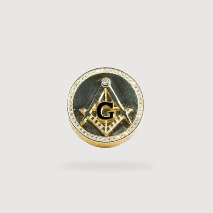 Inspired by the Mason Ring – Solid 10k Gold, this gold and black circular pin showcases Masonic symbols—a square and compass with a “G”—ringed by clear stones, echoing classic details of the Mason ring.