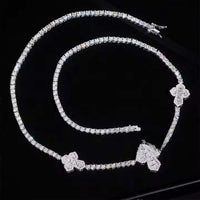 The Iced Out Moissanite Cross Tennis Chain - 3mm and its matching bracelet, both featuring cross-shaped pendants, shimmer elegantly on a glossy black surface.