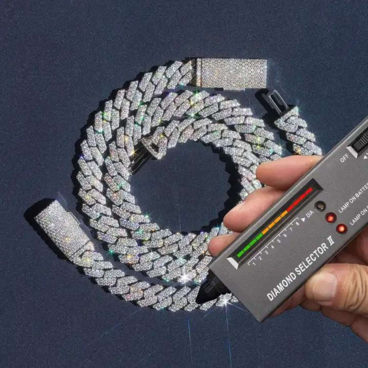 A hand uses a diamond tester on the Moissanite Cuban Link Chain 10mm - 925 Sterling Silver, its sparkling stones glowing as the tester’s lights confirm their brilliance on a dark surface.