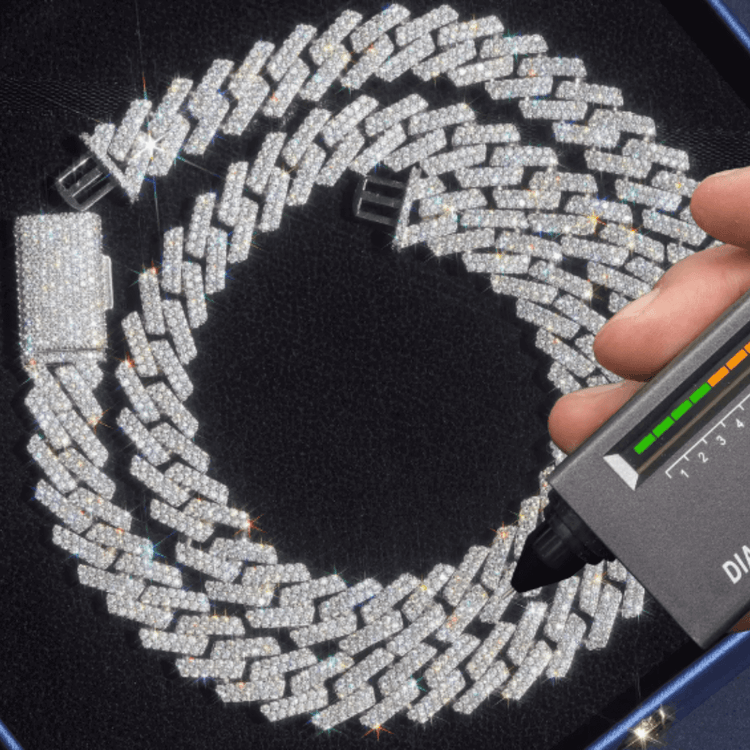 A hand uses a diamond tester on the Moissanite Cuban Link Chain 15mm - 925 Sterling Silver, its stones sparkling brilliantly against a dark background. The tester’s lights confirm the chain's authenticity.