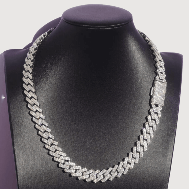 The Moissanite Cuban Link Chain 15mm - 925 Sterling Silver features a diamond-encrusted pattern and clasp, displayed on a black velvet jewelry bust against a plain background.