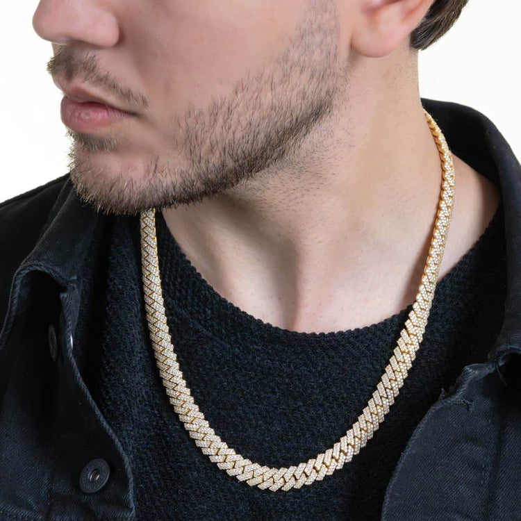 A man with light facial hair wears a black textured sweater, a black denim jacket, and a Moissanite Cuban Link Chain 8mm-23mm - Solid Yellow Gold alongside a thick gold chain. The image highlights his lower face, neck, and upper chest.