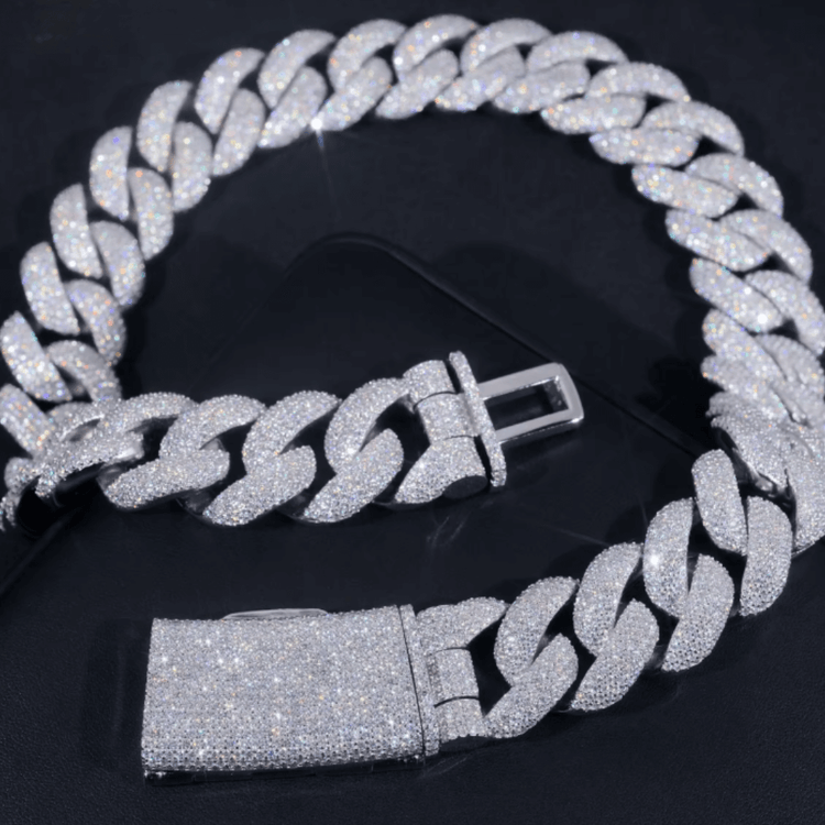The Moissanite Cuban Links Chain 25mm in 925 Sterling Silver is displayed on a dark surface with its open clasp visible, sparkling brightly under the light and highlighting its dazzling brilliance.