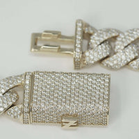 A close-up of the 13mm Natural Diamond Cuban Link Chain shows its solid 10k gold links and rectangular clasp, both encrusted with sparkling natural diamonds, displayed against a plain, light background.