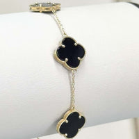 The Onyx Four Leaf Clover Bracelet in 14k yellow gold features two onyx clover-shaped charms with beaded gold borders, displayed on a white stand—perfect as good luck jewelry.
