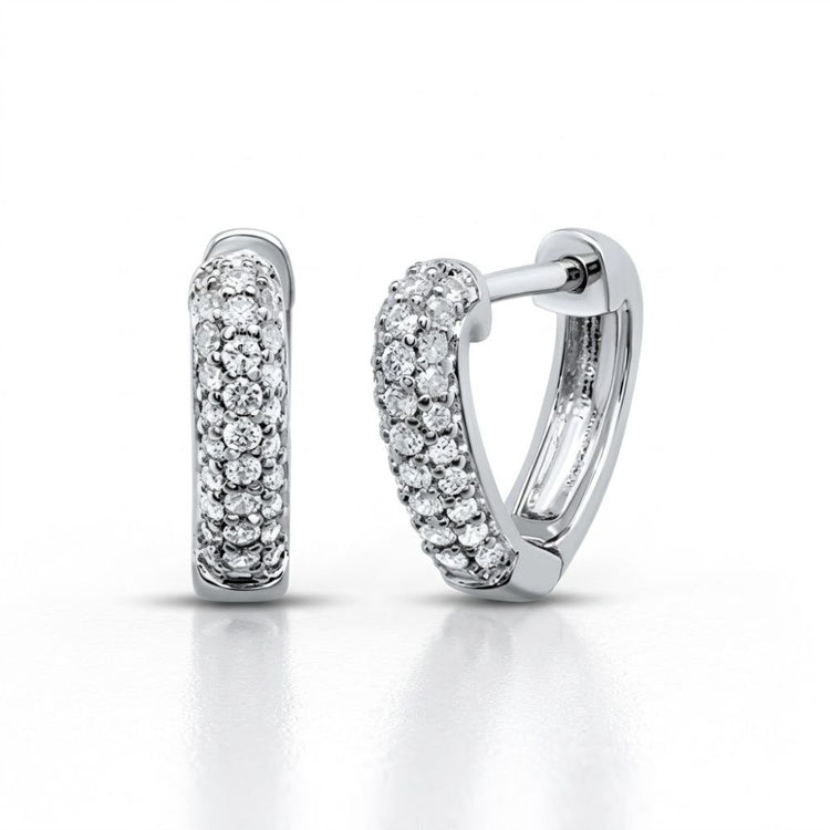 The 10K White Gold Diamond Heart Huggie Hoop Earrings are shown on a white background, with one earring upright and the other on its side to display the latch-back closure. Both feature small round diamonds for added sparkle.