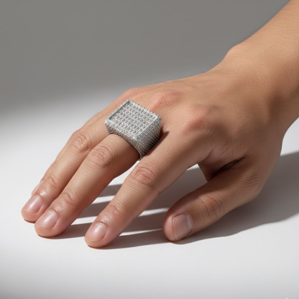 A hand displays the Iced-Out Square Baguette Signet Ring – 7.20 CT, a men's diamond ring with a textured, grid-like surface, against a plain light background.