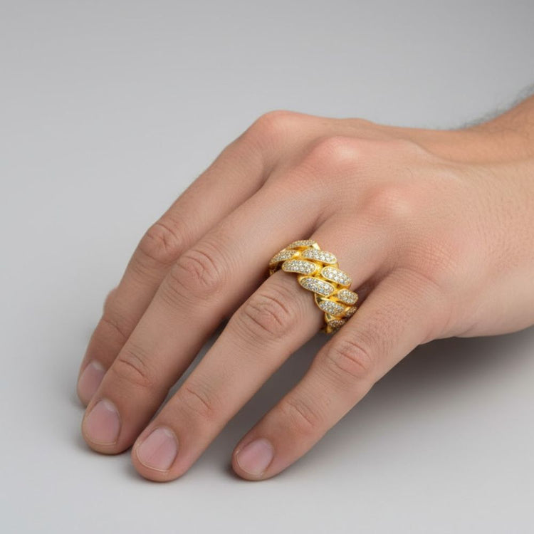 A hand showcases the 14k - 10mm - Iced Cuban Link Ring in Solid Gold, featuring rows of sparkling white stones, set against a plain light gray background.