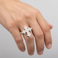 A hand with light skin tone wears the 10k Pincky Natural Diamond Cross Ring, a large silver piece adorned with sparkling stones, on the middle finger against a plain light background.