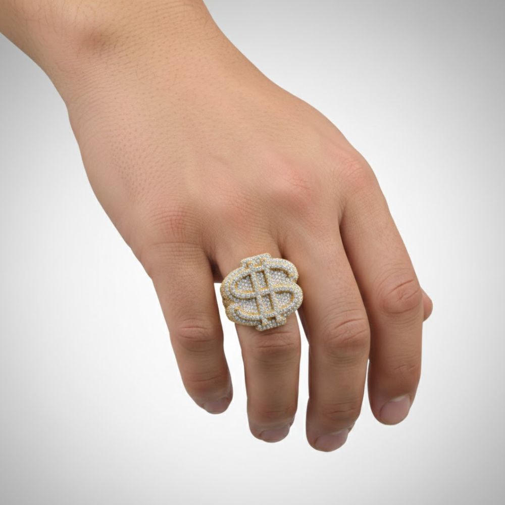 A hand wears the Dollar Sign Diamond Ring – 4.32 CT Pavé Design on the middle finger, its sparkling style catching the light against a plain background—ideal for fans of unique gold diamond rings.
