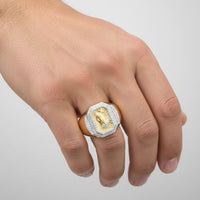 A hand displays the 1/2CTW Diamond Praying Hands Cross Men’s Ring in 10k gold, featuring an engraved praying hands cross and a border of small clear stones, set against a plain, light-colored background.