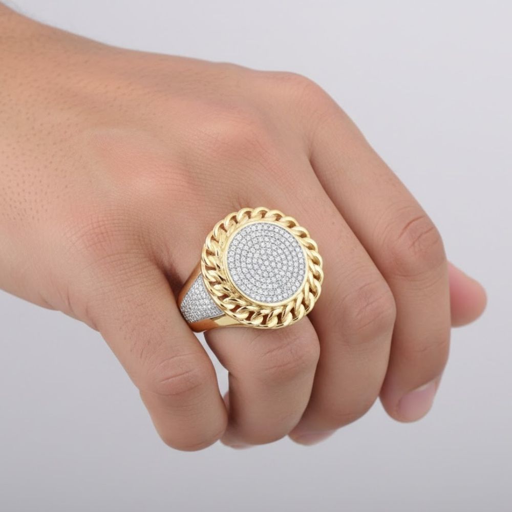 A hand displays the 10K Yellow Gold Diamond Cuban Link Ring 1/2CT, featuring a round diamond face with a twisted gold border and sparkling accents, shown against a simple light background.