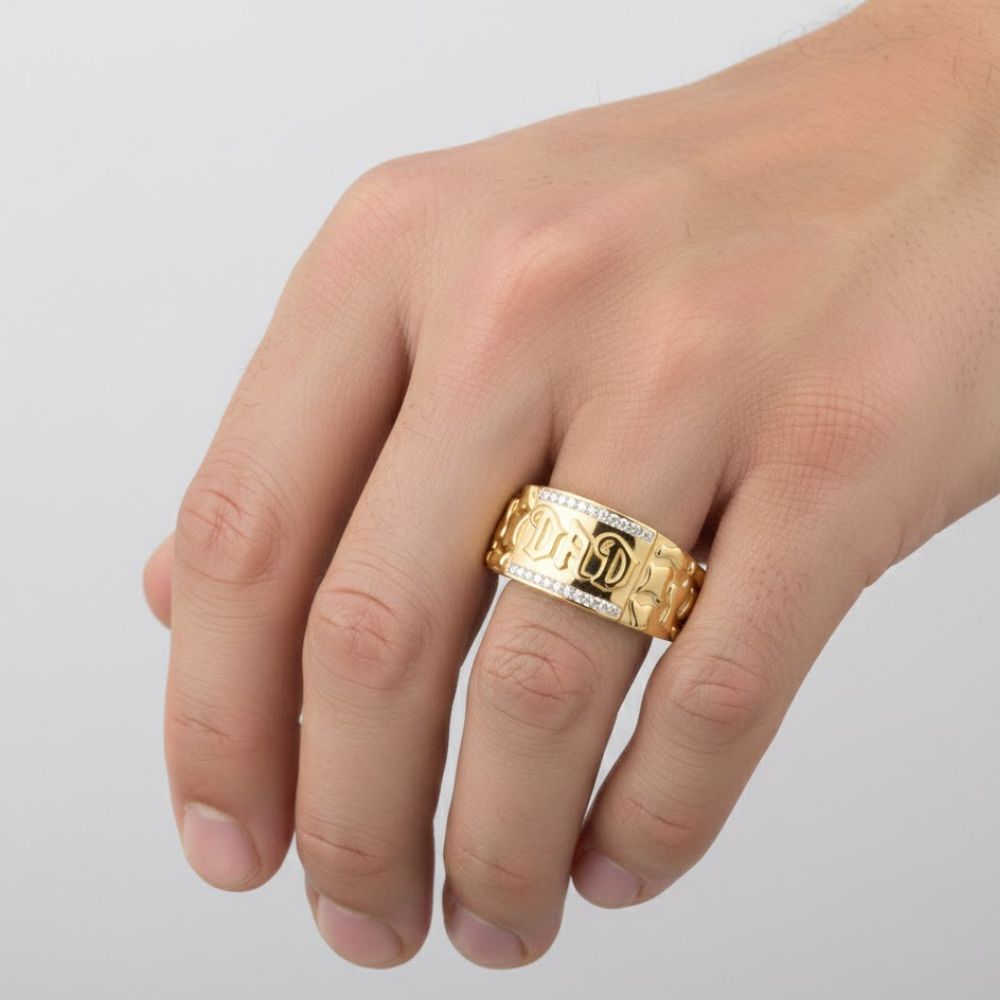 A hand wears a thick 10k gold Dad men's ring with natural diamonds on the middle finger. The ring features elegant silver detailing, making it an ideal Father’s Day gift. The background is plain and light-colored.