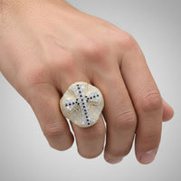 A hand displays the 10k Gold Diamond Cross Men's Ring 2 7/8 Cttw, featuring a cross of sparkling white and black diamonds atop bold yellow gold, standing out prominently on the finger against a plain background.