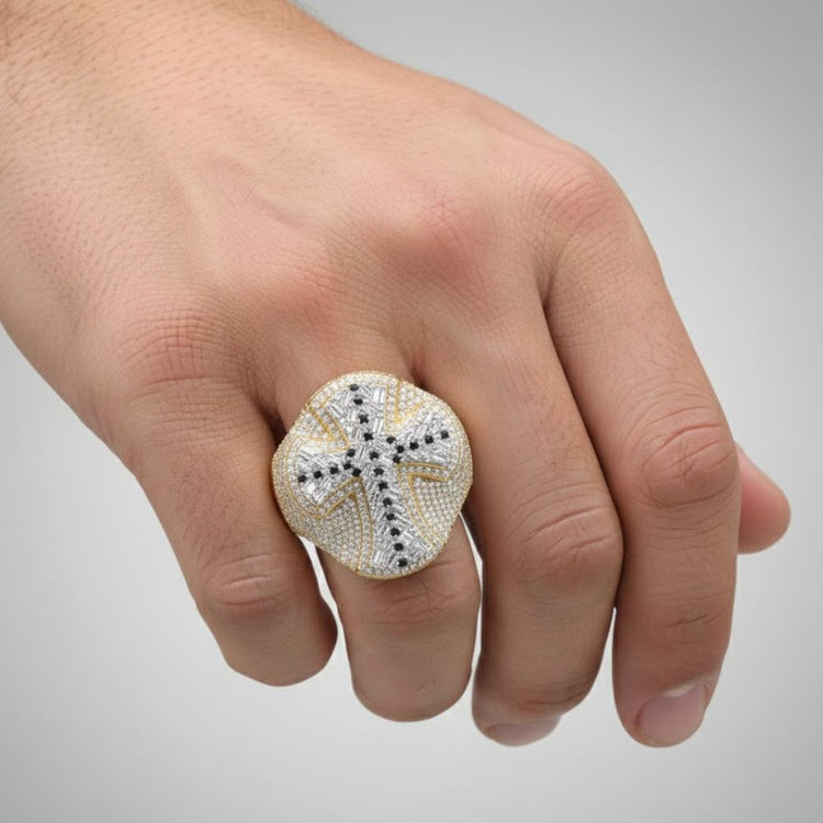 A hand displays the 10k Gold Diamond Cross Men's Ring 2 7/8 Cttw, featuring a cross of sparkling white and black diamonds atop bold yellow gold, standing out prominently on the finger against a plain background.