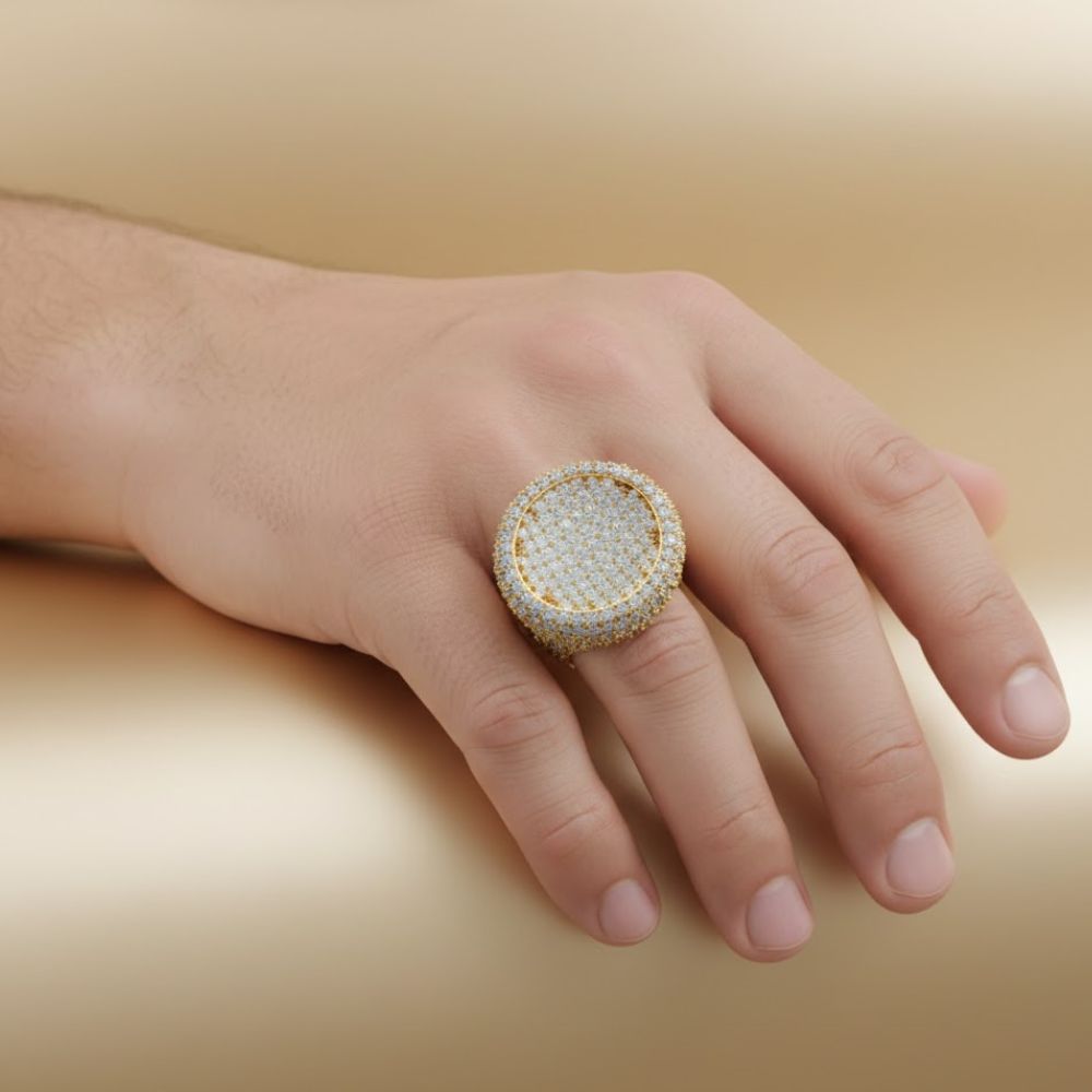A hand rests on a smooth, beige surface, adorned with the Round Pavé Diamond Ring – 14.11 CT Gold Design—a standout gold men's ring encrusted with pavé diamonds.