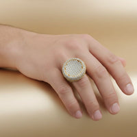 A hand rests on a smooth, beige surface, adorned with the Round Pavé Diamond Ring – 14.11 CT Gold Design—a standout gold men's ring encrusted with pavé diamonds.