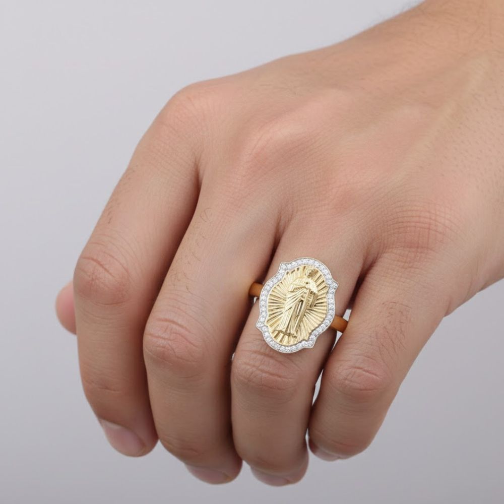 A hand wears a 10k Yellow Gold St. Jude Diamond Ladies Ring (1/5 Cttw) with an oval face, raised St. Jude figure, and a border of sparkling diamonds against a plain light background.