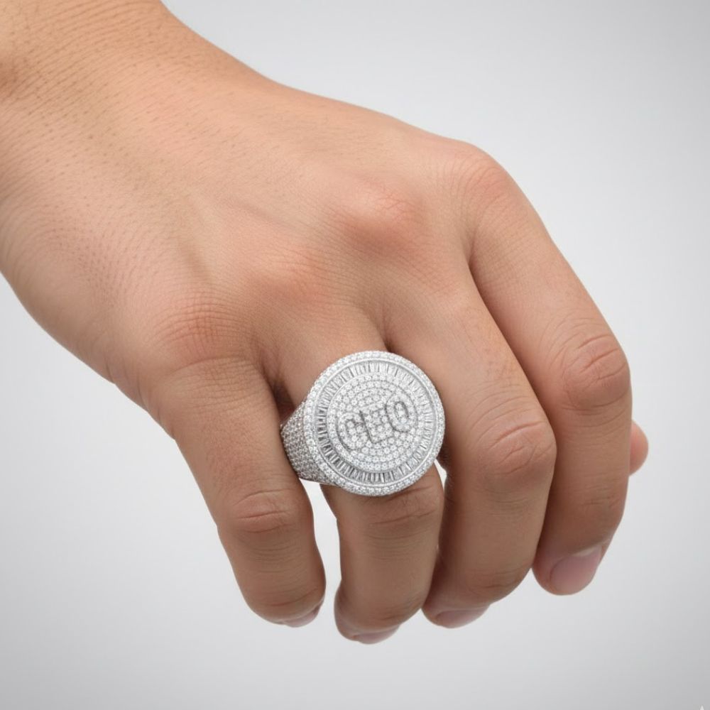 A hand wears the Baguette Moissanite CEO Round Head Fashion Ring, featuring a large round silver setting with diamond accents and "CEO" in the center, shown against a plain light background.