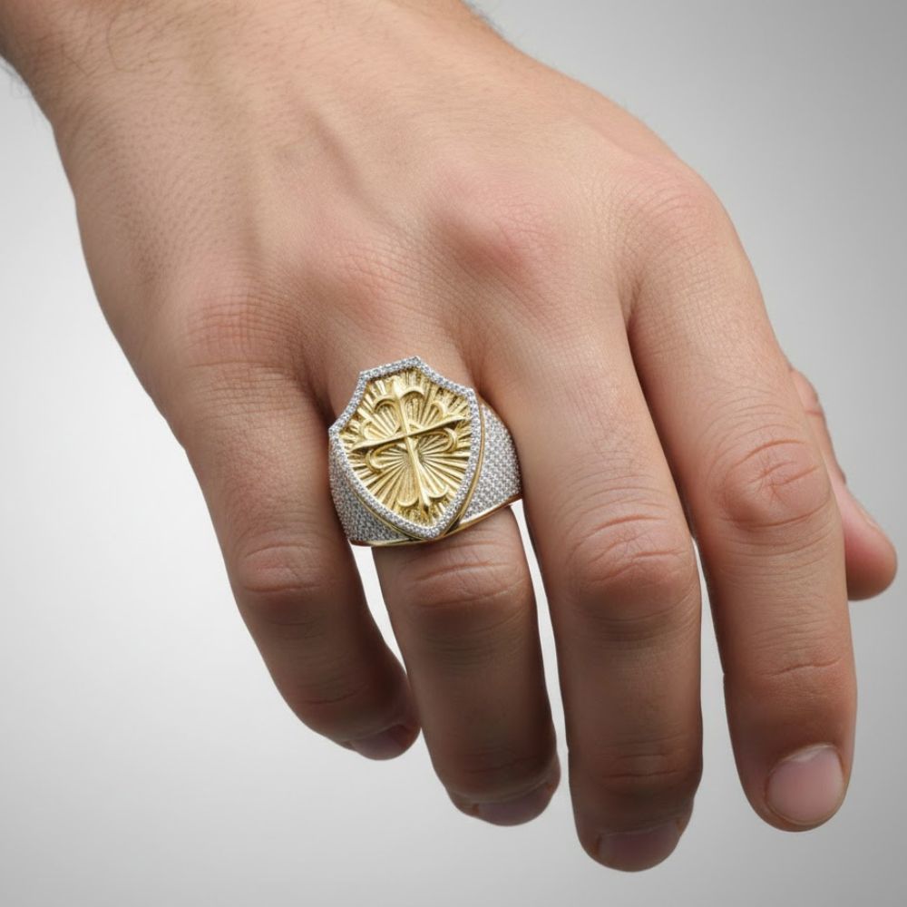 A hand displays the 10k Gold 7/8 CTTW Diamond Cross Men’s Ring, featuring a shield-shaped design with raised diamond cross pattern and silver band, set against a plain light background.