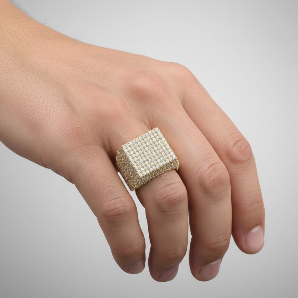 A hand displays the Cube Pavé Diamond Ring – 5.50 CT Men's Gold Design, featuring a bold gold band with cube pavé sparkling diamonds on the ring finger, set against a plain gray background.
