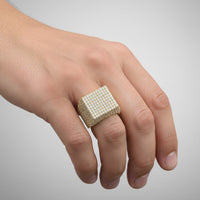 A hand displays the Cube Pavé Diamond Ring – 5.50 CT Men's Gold Design, featuring a bold gold band with cube pavé sparkling diamonds on the ring finger, set against a plain gray background.
