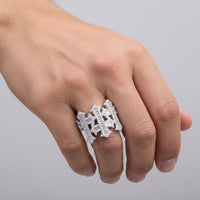 A hand wears the Baguette Moissanite Cross Religious Ring, a large silver piece with geometric designs and pavé moissanite stones, shown on middle and ring fingers against a plain light gray background.