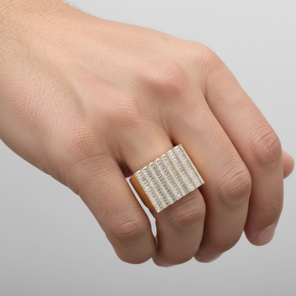 A hand wears the Baguette Stack Diamond Ring – 1.56 CT Gold Design, a large rectangular men's ring featuring rows of sparkling clear stones. The background is plain light gray.