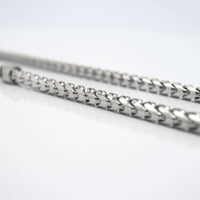 Close-up of two shiny, interlocking zigzag rods resembling the Franco Chain White Gold - 10k 3.5MM Ready to Ship, placed parallel on a reflective white surface with a sharp front focus and blurred background.